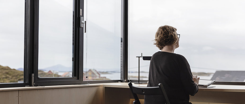woman at desk in front of large windows looking out over coastline view
