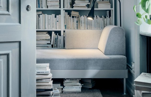 tiny room with IKEA delaktig sofa, full bookshelves, books on the floor.