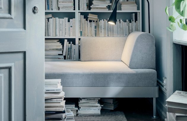 tiny room with IKEA delaktig sofa, full bookshelves, books on the floor.