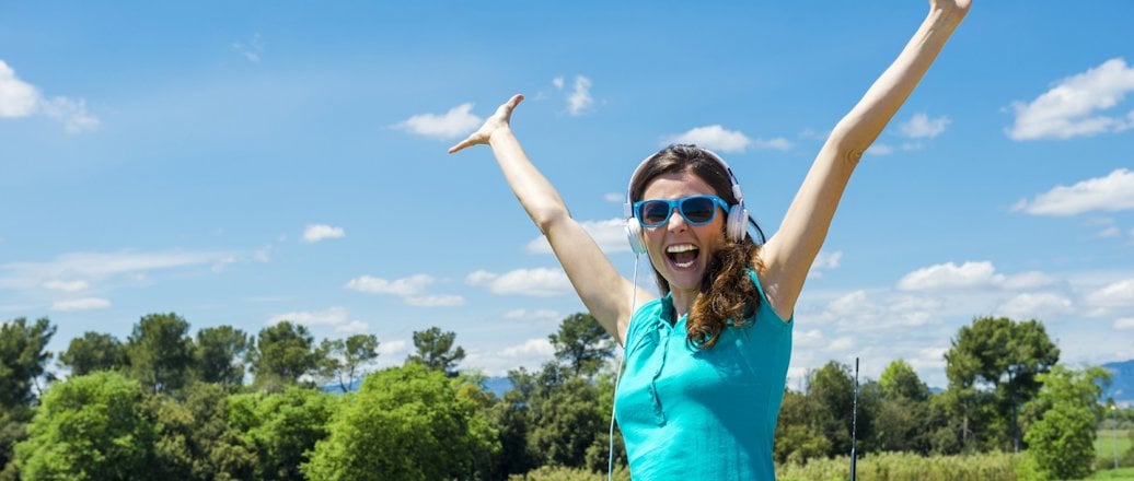 cheerful young woman wearing sunglasses and raised hands on the sunroof of a car