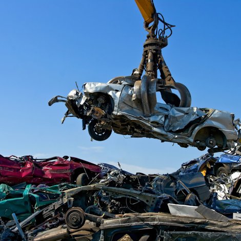 Large crane holding wrecked car over heap of scrap metal