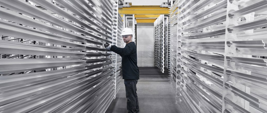 Worker inspecting long extruded rods of aluminium on shelves